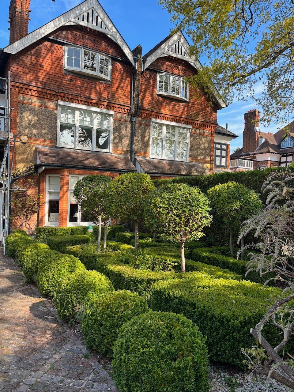 Brick Victorian house with arched gables and bay windows, surrounded by manicured green hedges and topiary in the front garden
